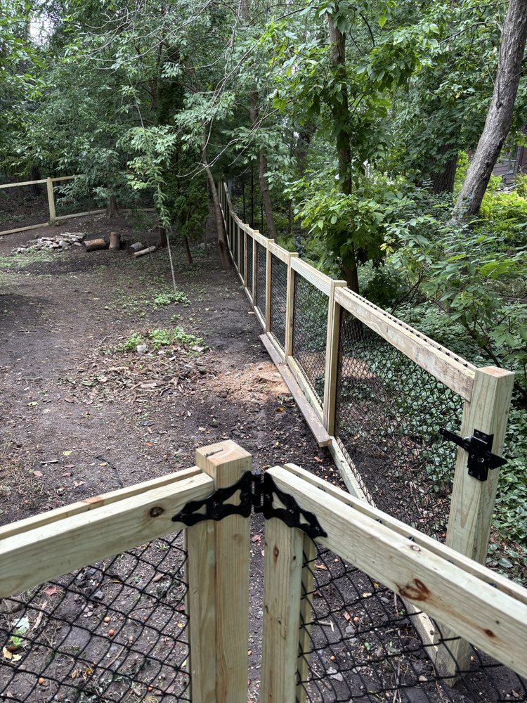 Black chainlink fence with a cedar-framed gate winding through a wooded lot