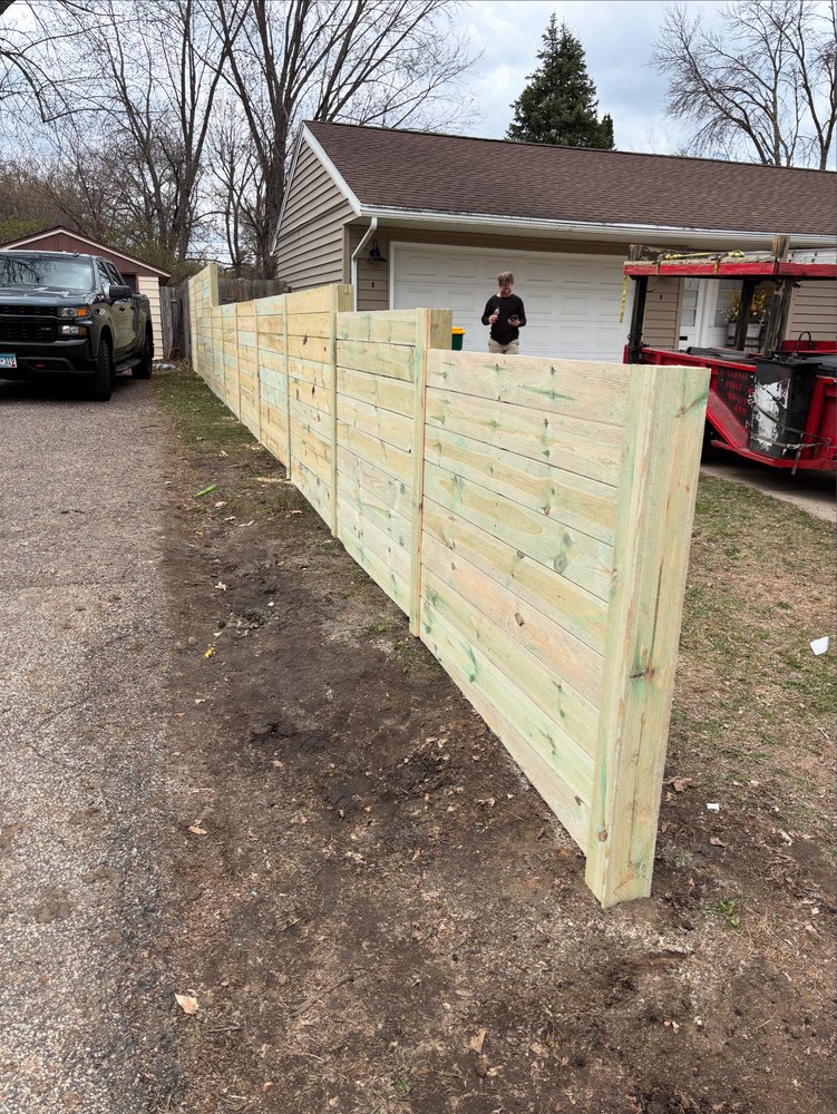 A long treated-pine horizontal fence run laid straight along a driveway